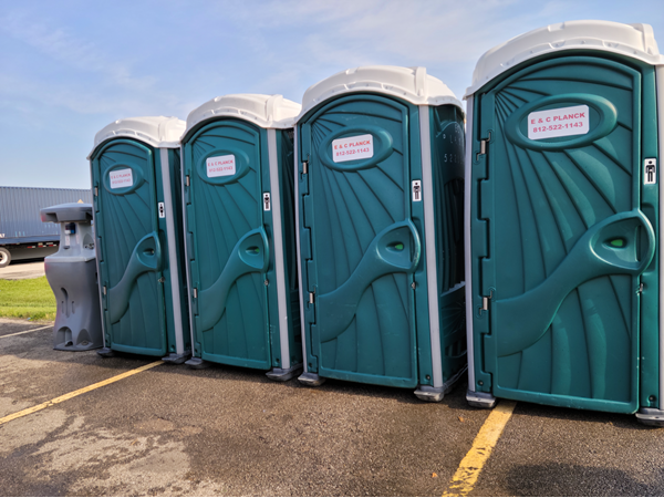 A row of green portable toilets are lined up in a parking lot