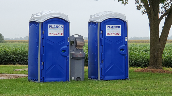 Two blue portable toilets are sitting next to each other in a grassy field.