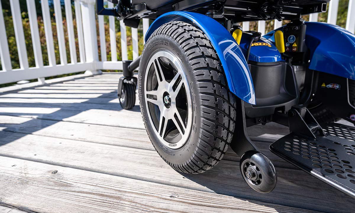 Close-up of a blue mobility scooter wheel on a wooden deck with white railing