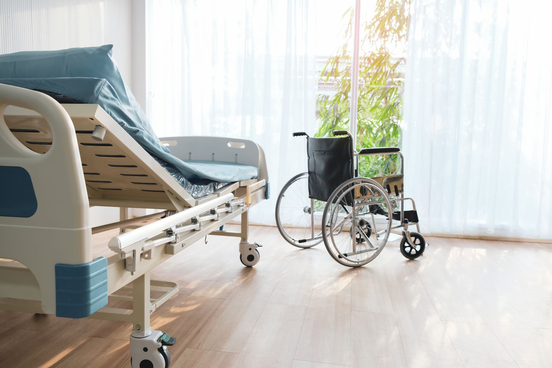 Hospital room with an empty bed and a wheelchair by a bright window