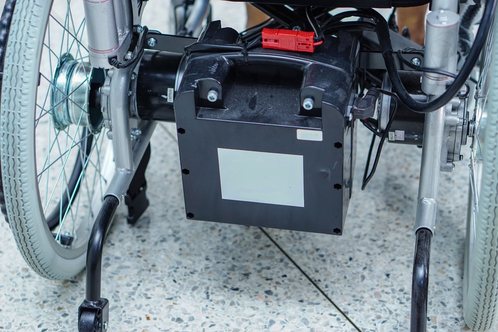 Close-up of a wheelchair’s back with a black battery box and red wiring indoors