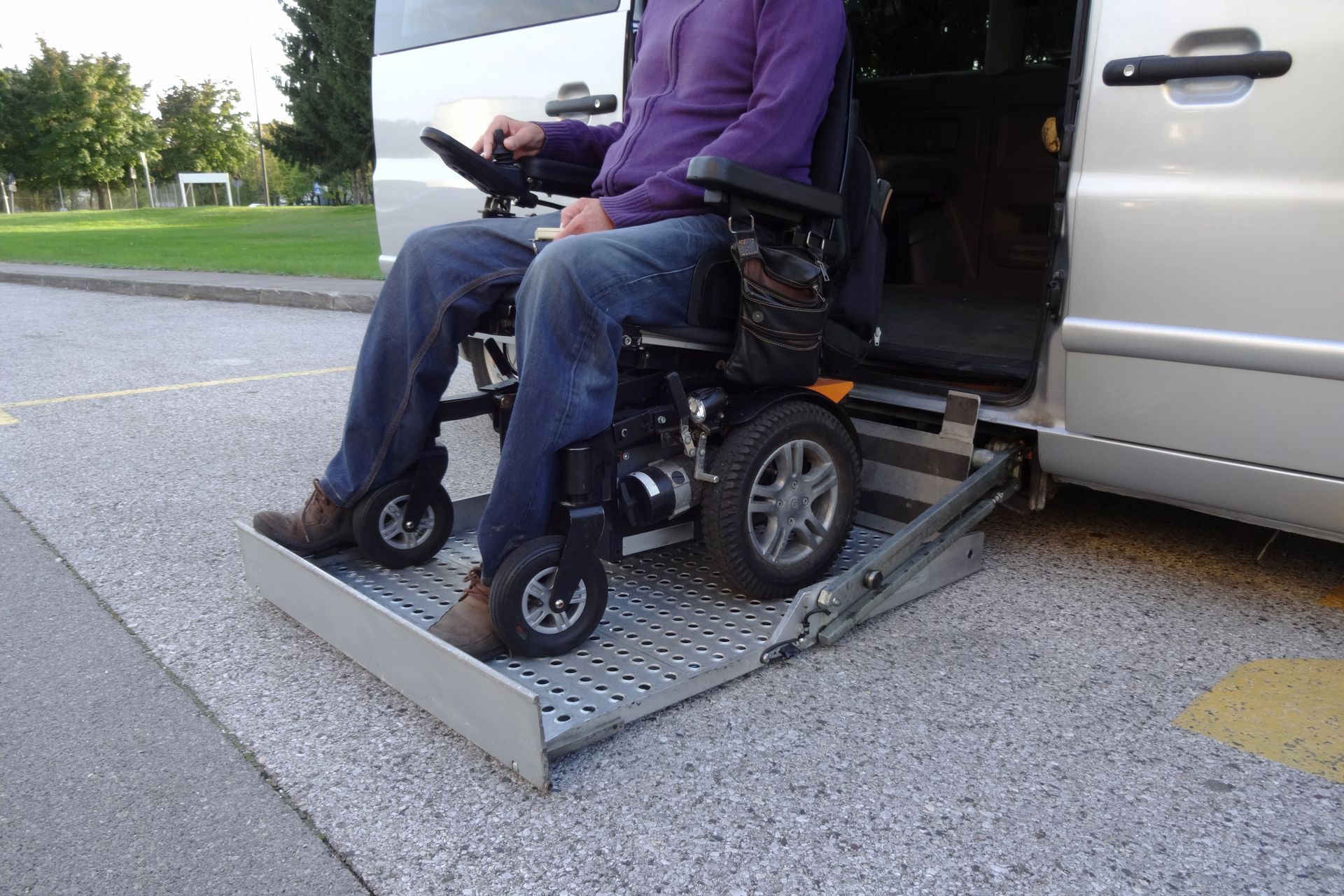 Person in a wheelchair using a ramp to enter a silver van.