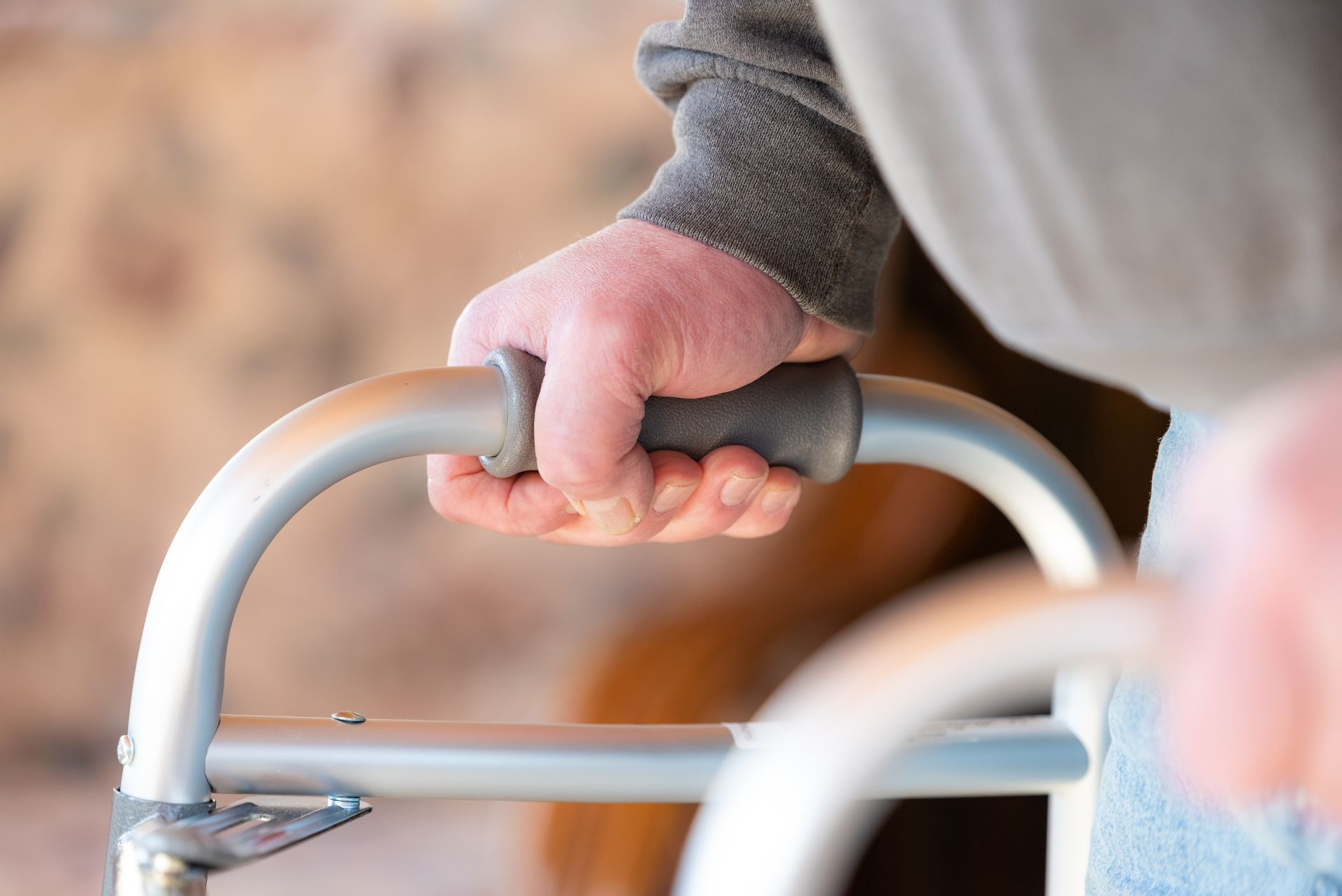 Hands gripping a gray walker handle, with a blurred beige background.