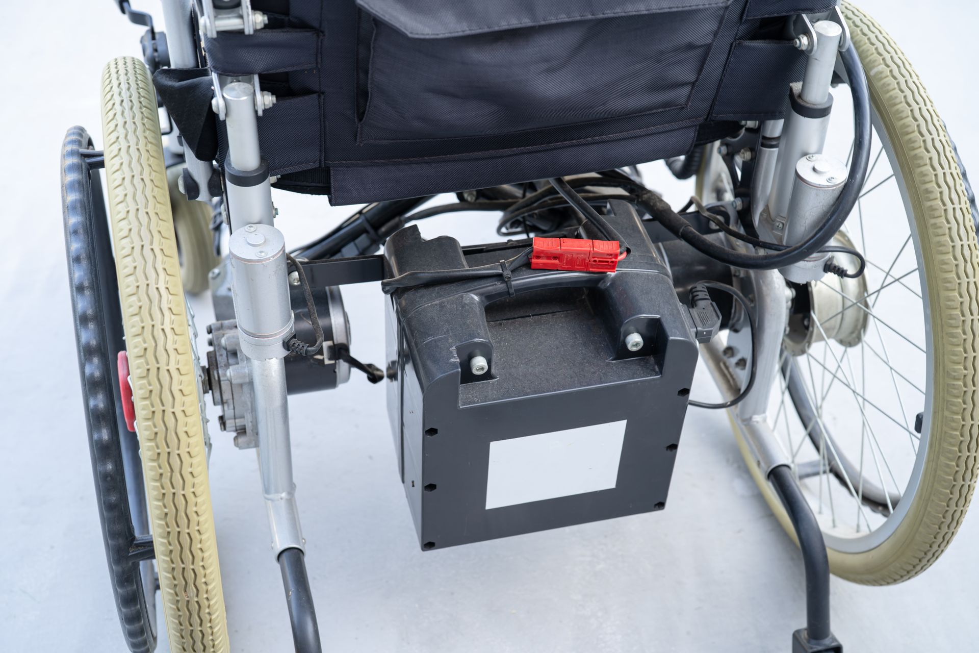 Close-up of a wheelchair with a black battery pack mounted beneath the seat.