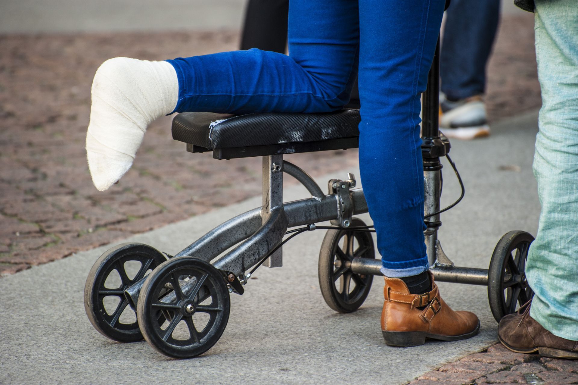 Person in blue pants with a white cast on one foot sitting on a wheelchair-like mobility cart outdoors