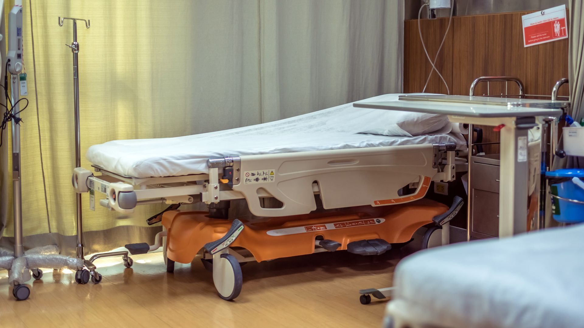 Hospital bed with white linens and orange stretcher wheels in a clinical room