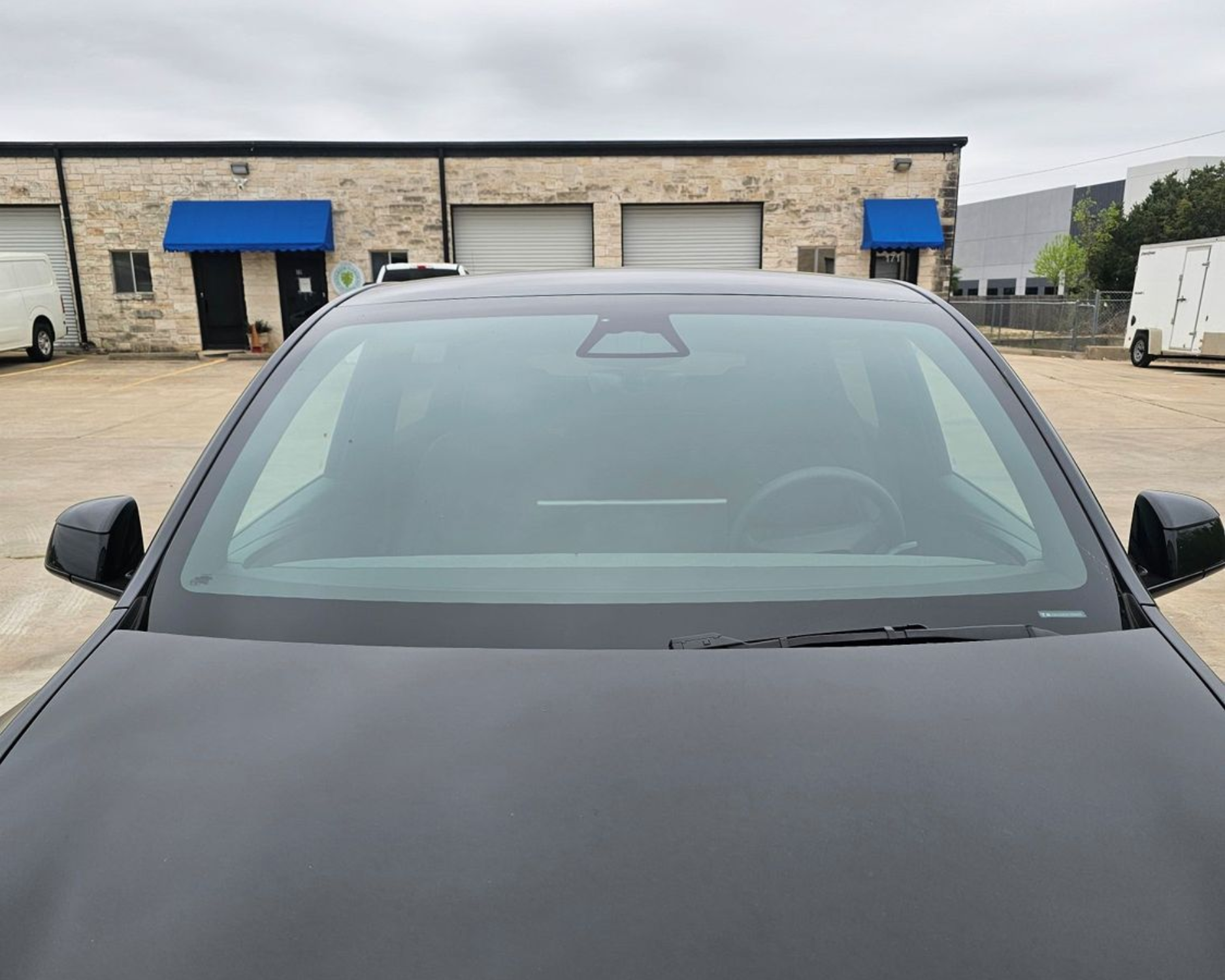 Black car parked in front of a warehouse with blue awnings