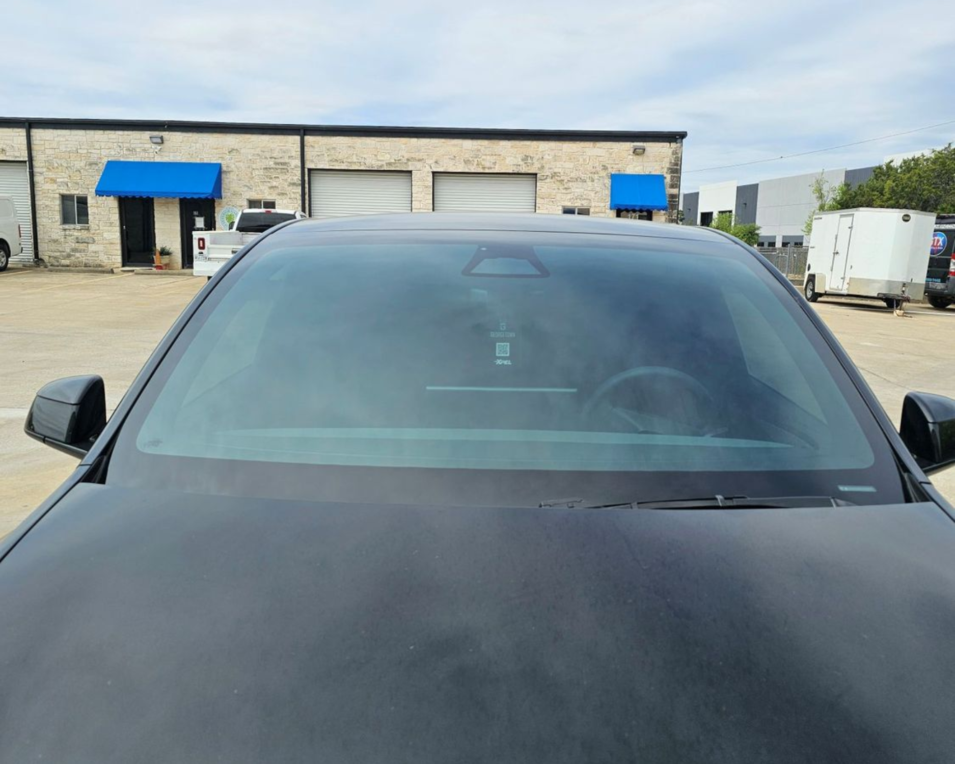 Front view of a black car parked in an industrial lot with warehouse buildings in the background