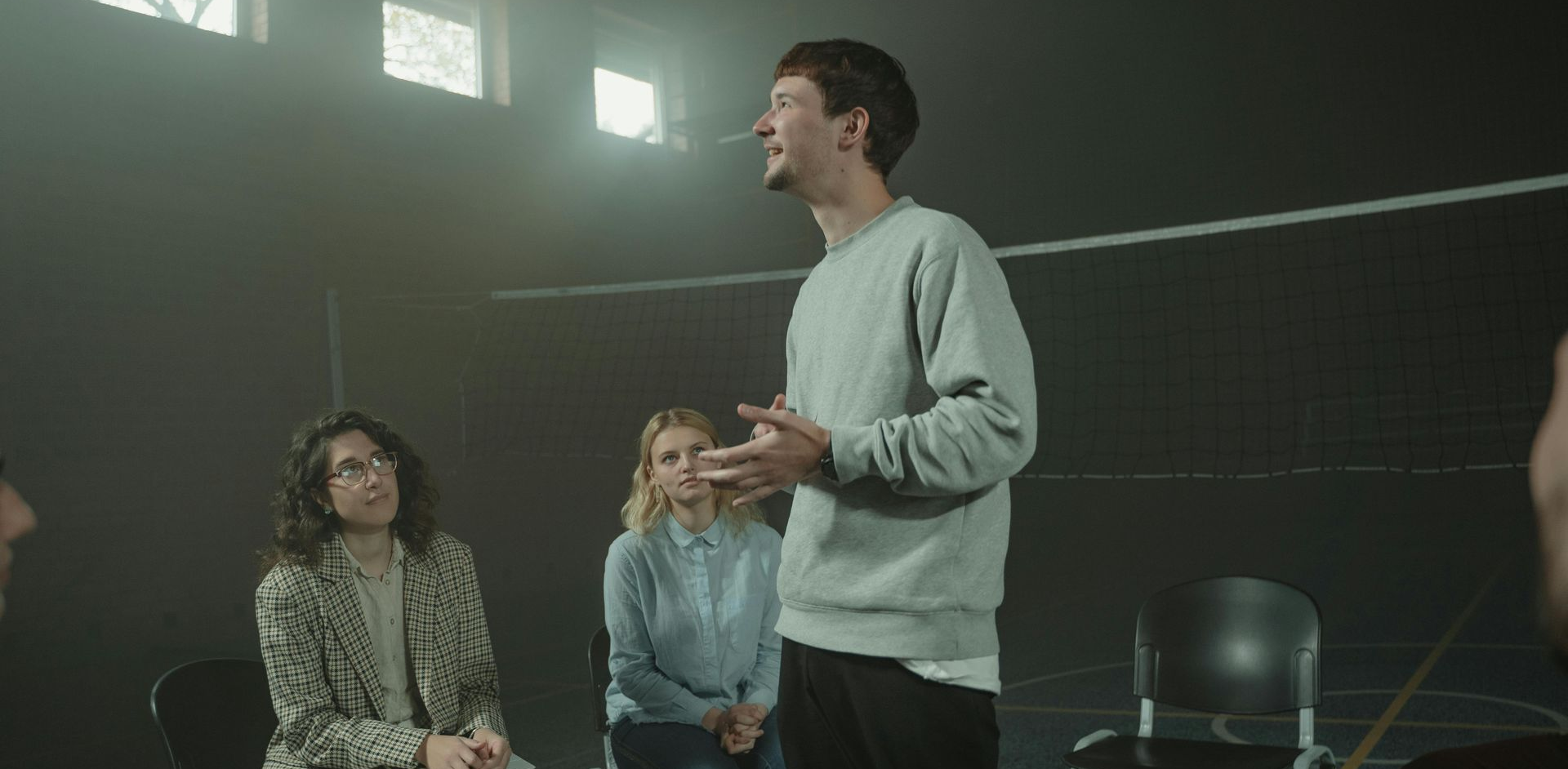 Man speaking to a seated group in a dim room, with two women listening nearby