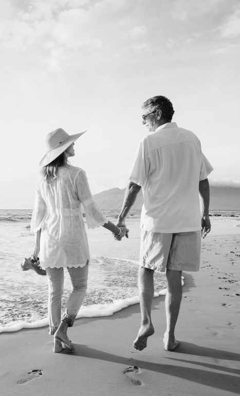 Couple holding hands walking along a beach at sunset, seen from behind