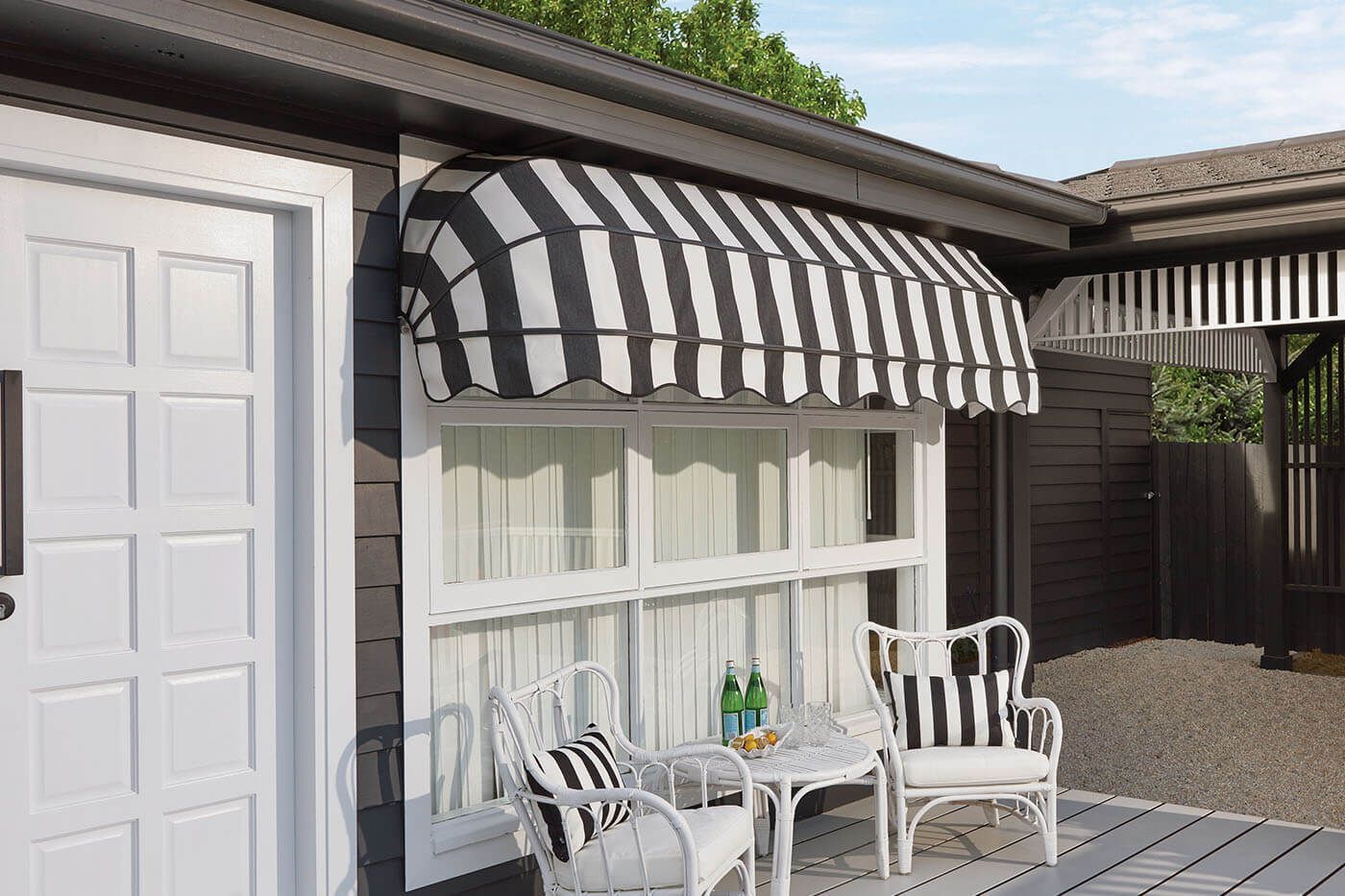 Black and white striped awning over a window with white furniture on a deck.