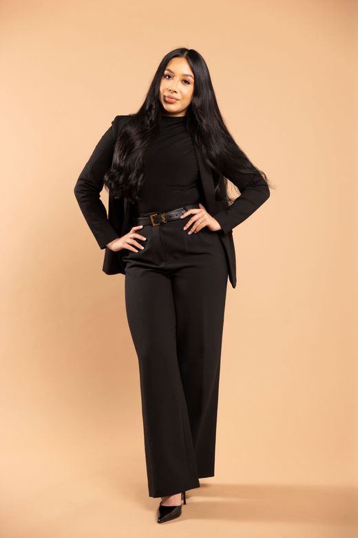 Woman in black suit posing against a beige studio backdrop.