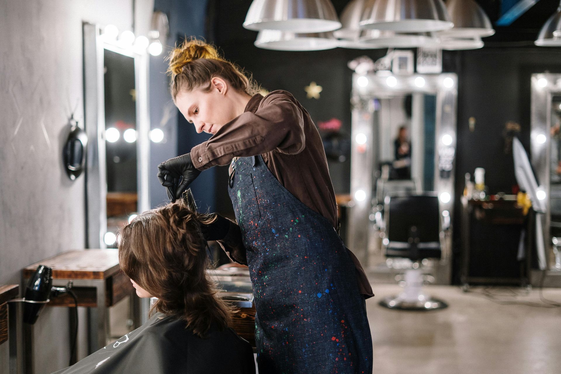 Hairdresser styling a client's hair in a modern salon with mirrors and lights.