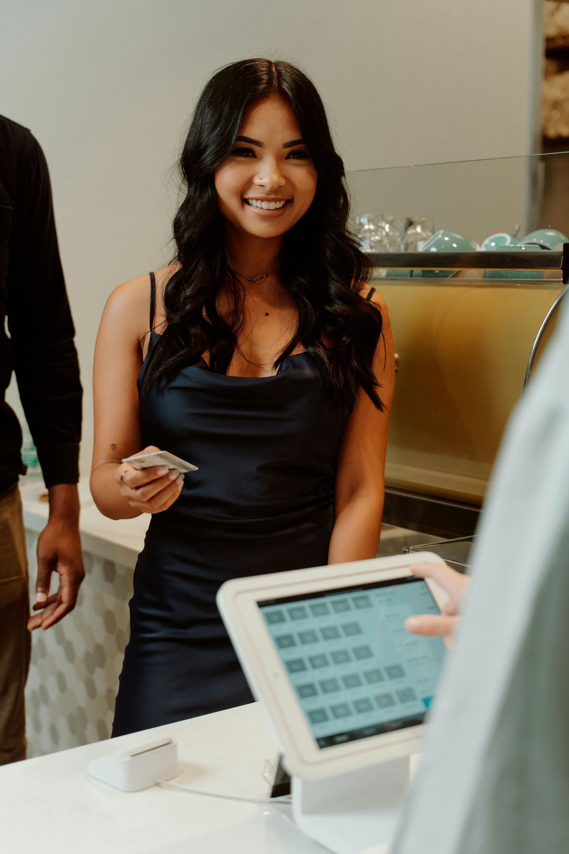 Smiling woman in a navy dress holding a card at an indoor event checkout counter
