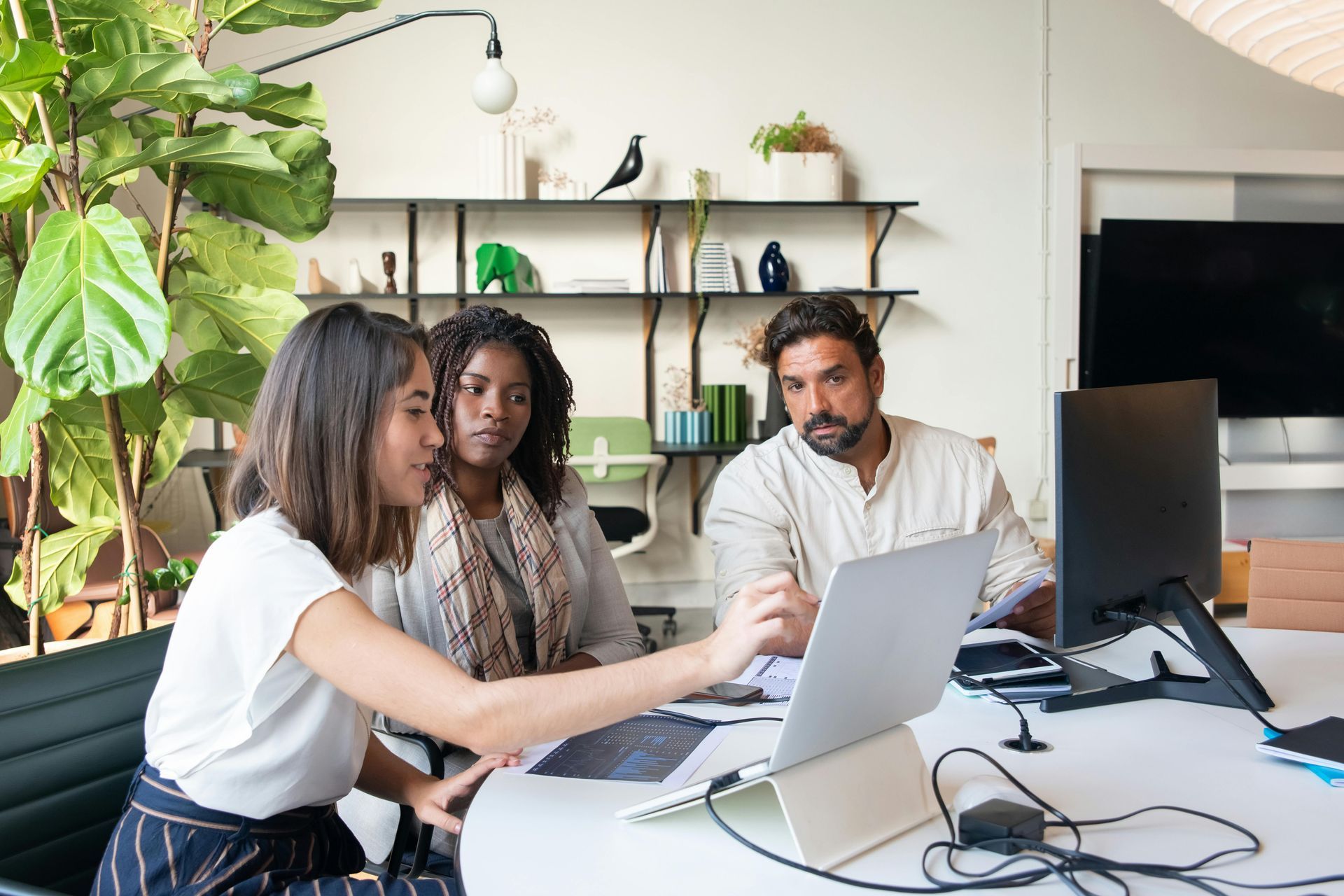 Three people collaborating at a desk with laptops in a bright office