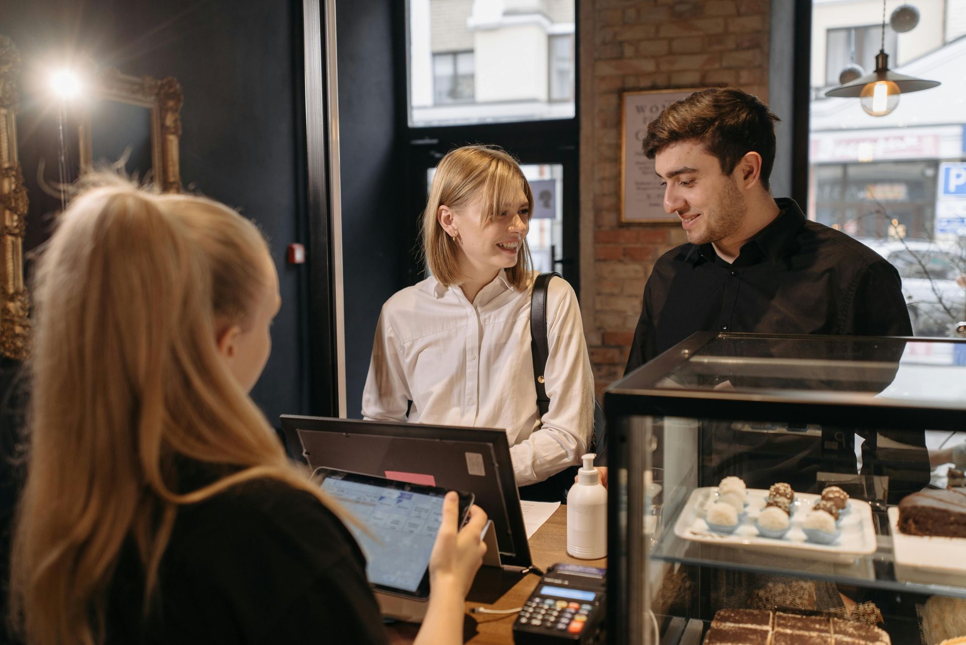 Cafe cashier serving two customers beside a pastry display case