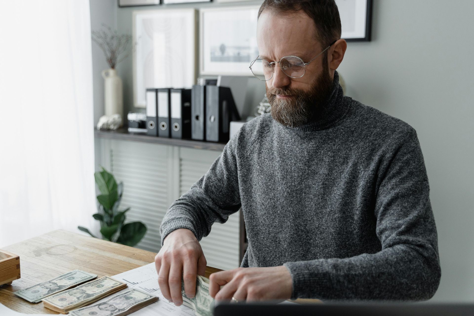 Man sorting papers at a desk in a bright home office with binders and a plant.