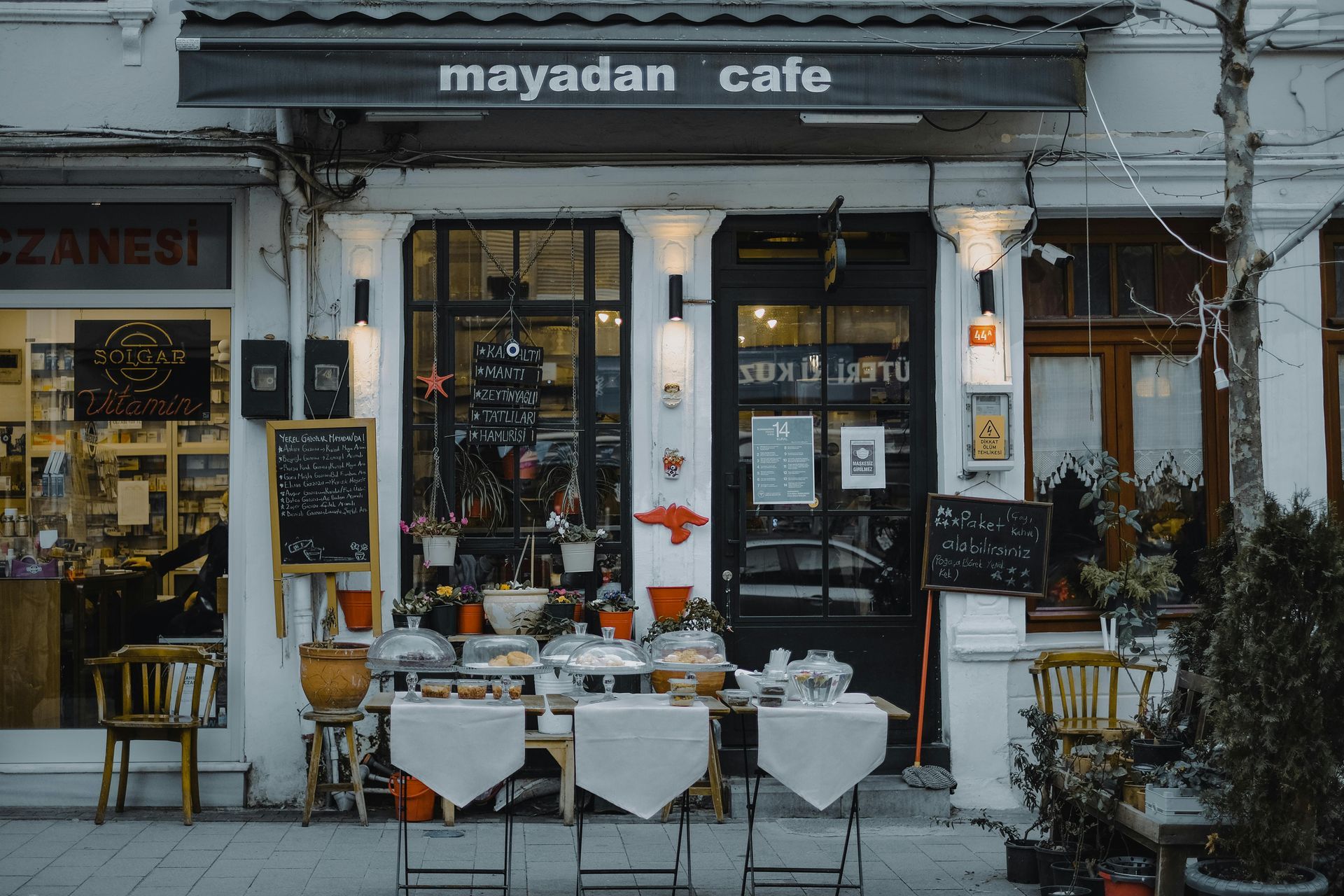 Mayadan Cafe storefront with outdoor seating, black and white facade, and potted plants