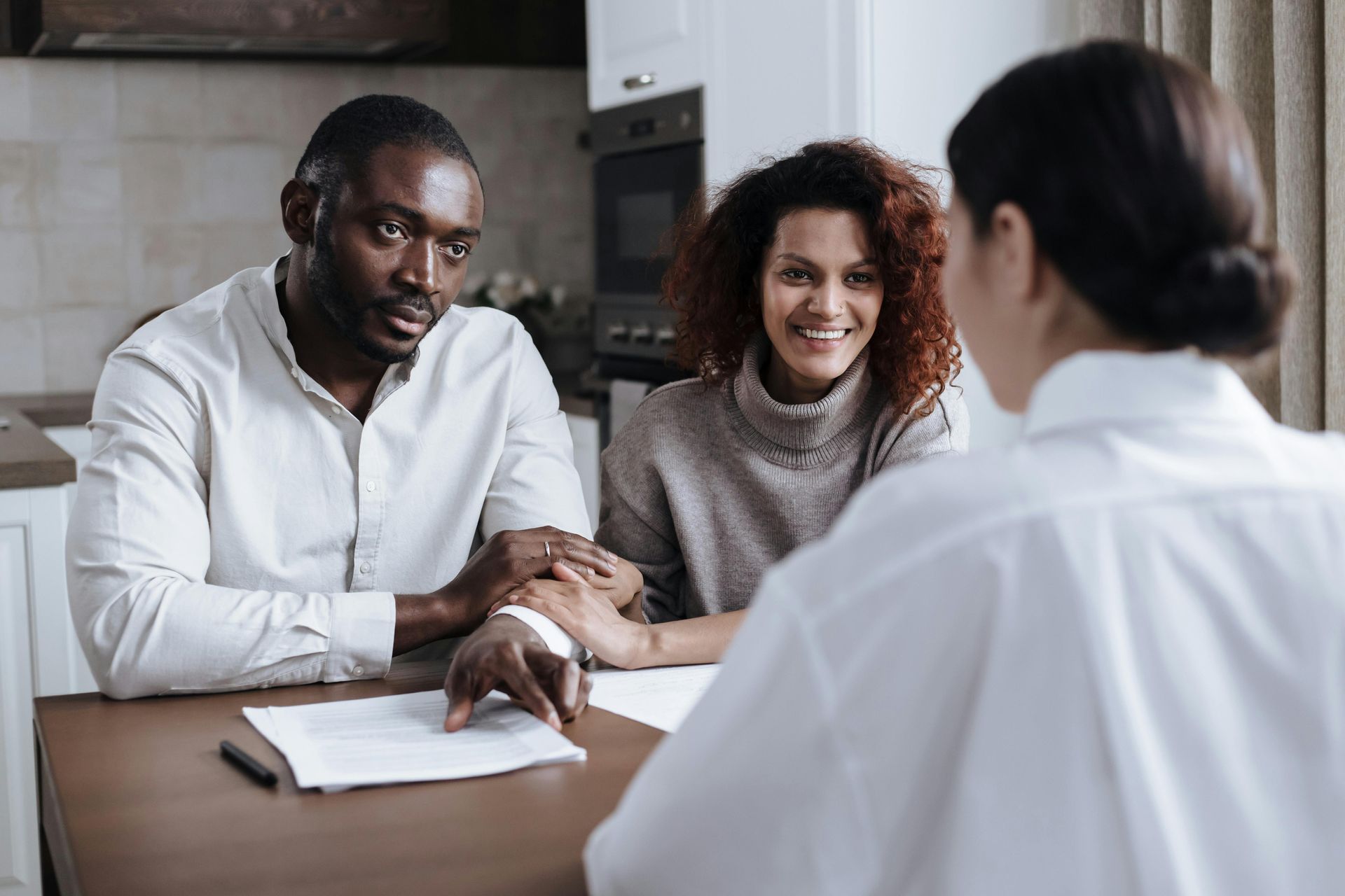 Two people meet with a consultant at a table, reviewing documents in a bright office.