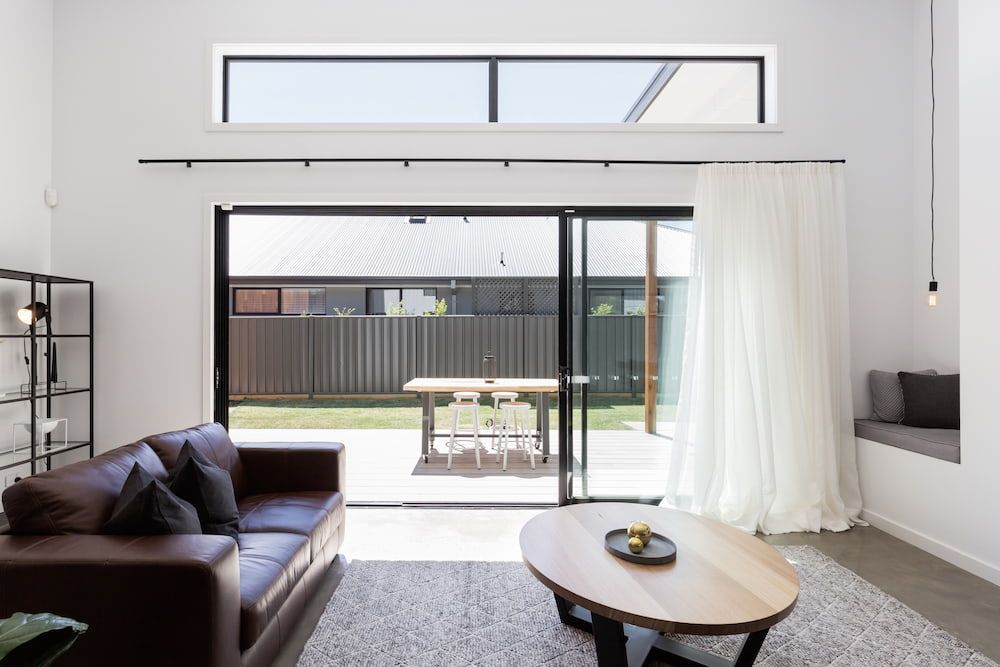 A Living Room With a Couch, Coffee Table, and Sliding Glass Doors Leading to a Patio — Curtain Force NQ in Garbutt, QLD