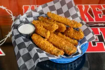 Basket of golden fried fish fillets with a white dipping sauce on a checkered paper-lined tray
