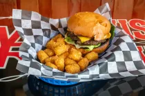 Burger and tater tots in a basket lined with black-and-white checkered paper