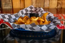 Basket of golden fried snacks in checkered paper on a table, with wood paneling in the background