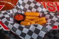 Basket of fried cheese sticks with marinara sauce on checkered paper-lined tray