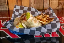 Taco wrap with fries in a checkered paper basket on a red tabletop