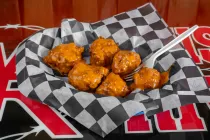 Basket of saucy buffalo wings in checkered paper with a fork on a red tabletop