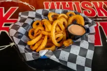 Basket of curly fries with a side of dipping sauce on a checkered paper-lined tray