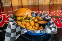 Cheeseburger with tater tots in a basket on a black table, with ketchup on the side