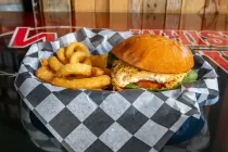 Burger and curly fries in a black-and-white checkered basket liner on a table.