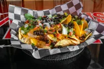 Loaded nachos with cheese, beans, sour cream, jalapeños, and herbs in a checkered basket.