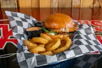 Burger and curly fries in a checkered basket liner with dipping sauce on a table.