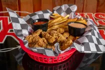 Basket of fried chicken and fries with dipping sauces on checkered paper liners