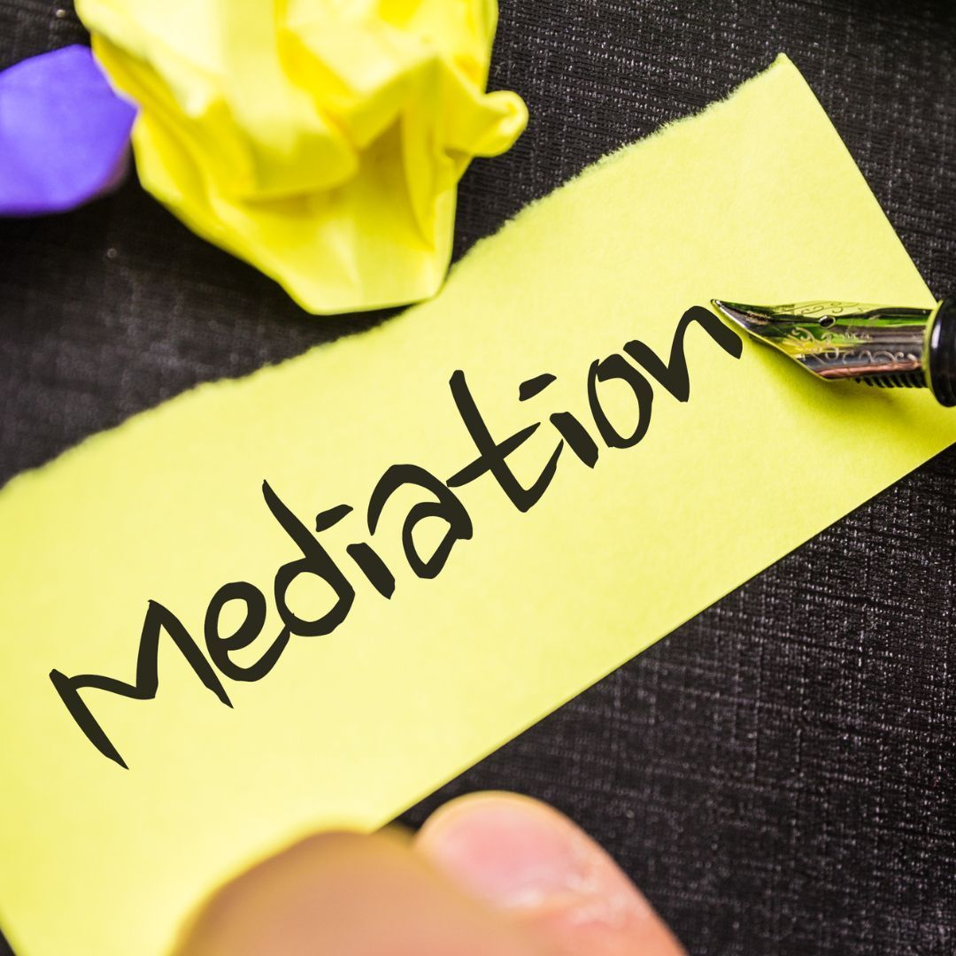 A person is writing the word mediation on a yellow sticky note