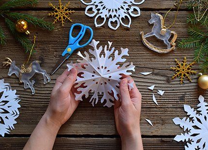 A person is making a paper snowflake with scissors on a wooden table.