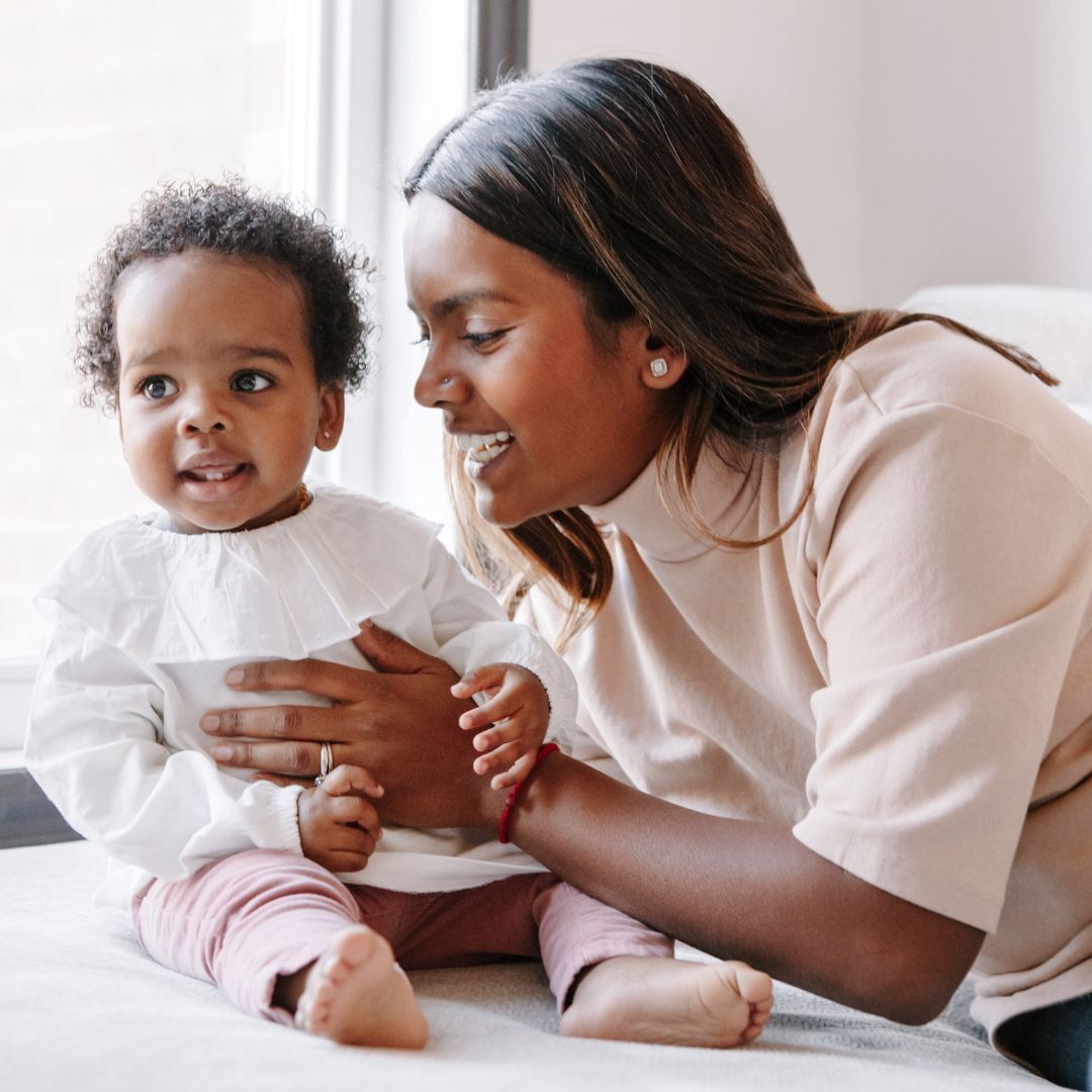 A woman is holding a baby while sitting on a bed.