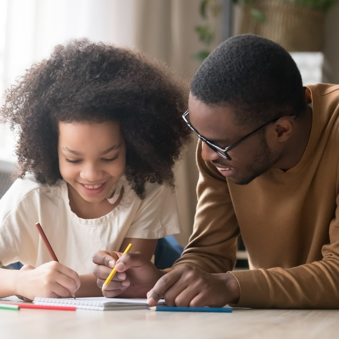A man and a girl are sitting at a table writing in a notebook.