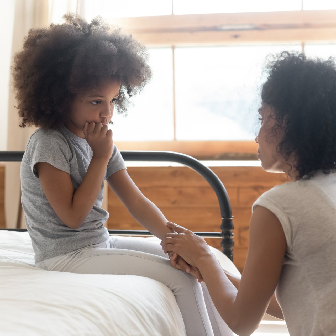A woman is talking to a little girl who is sitting on a bed