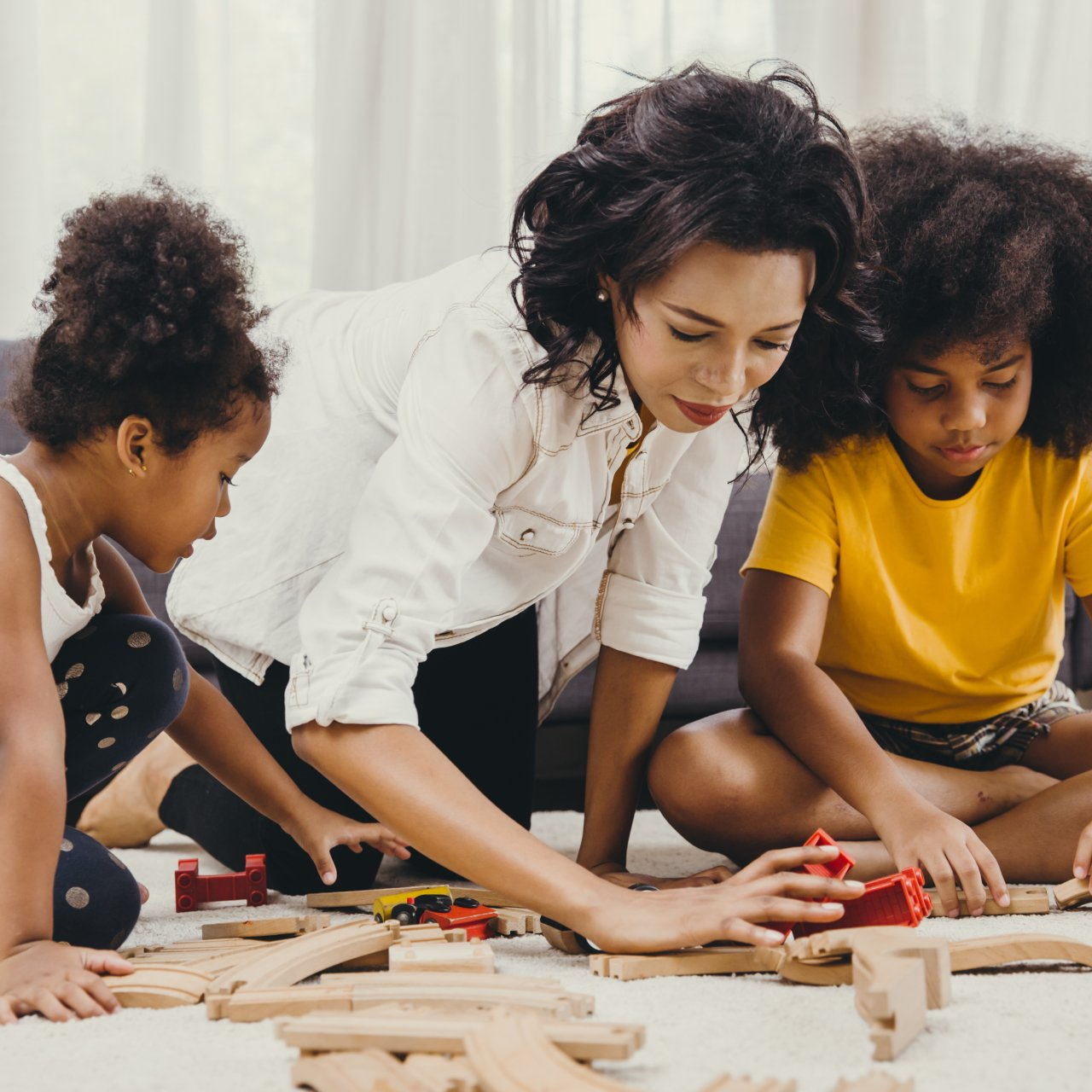 A woman and two children are playing with wooden blocks on the floor