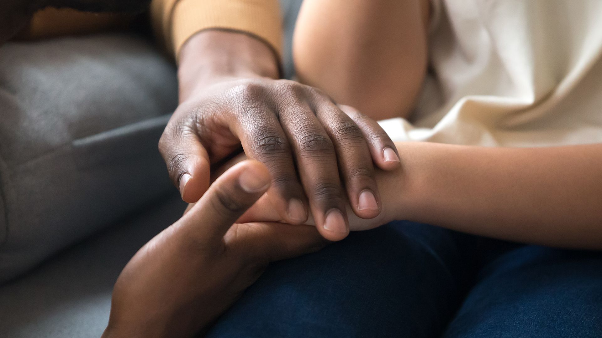 A man is holding a child 's hand while sitting on a couch.