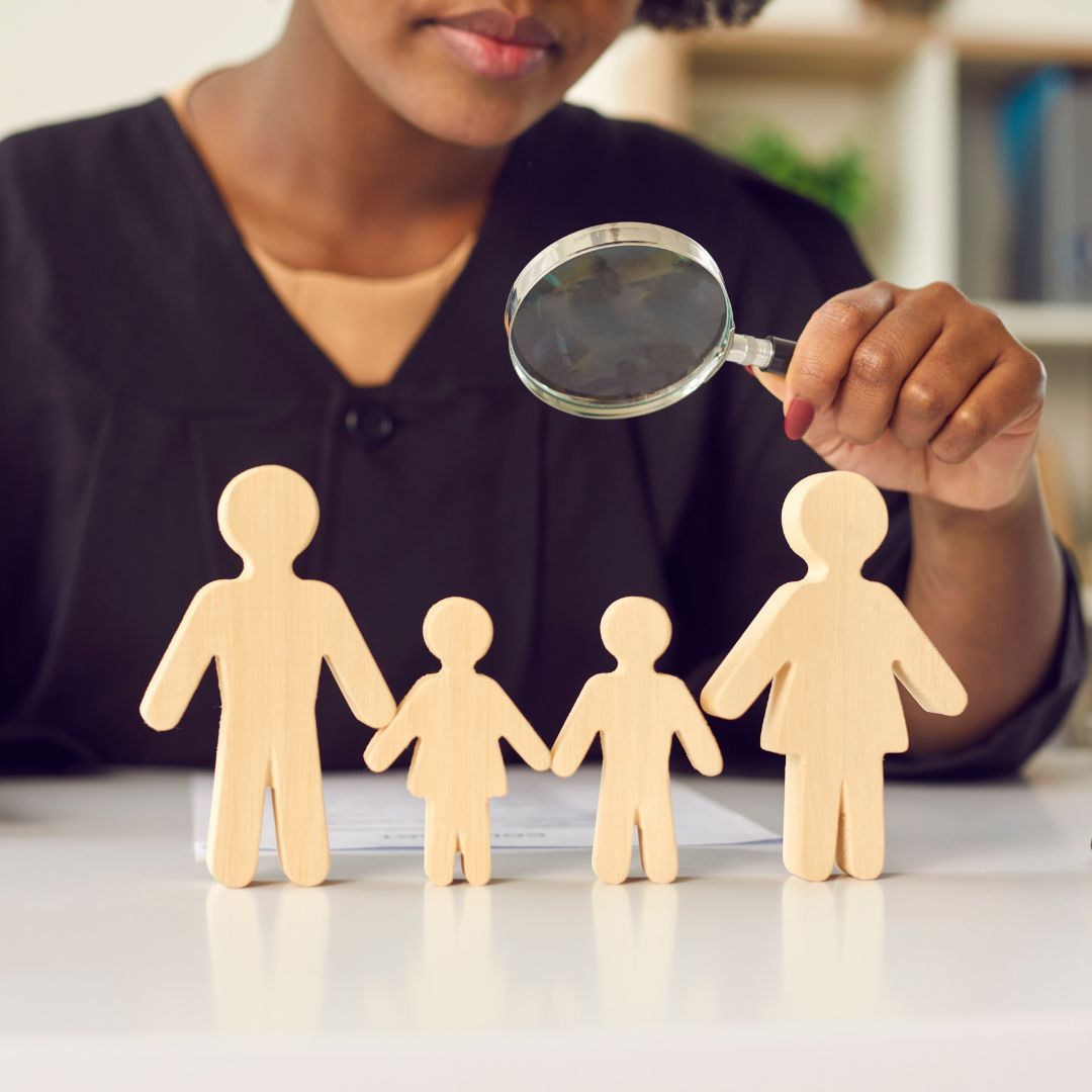 A woman is holding a magnifying glass over a group of wooden people