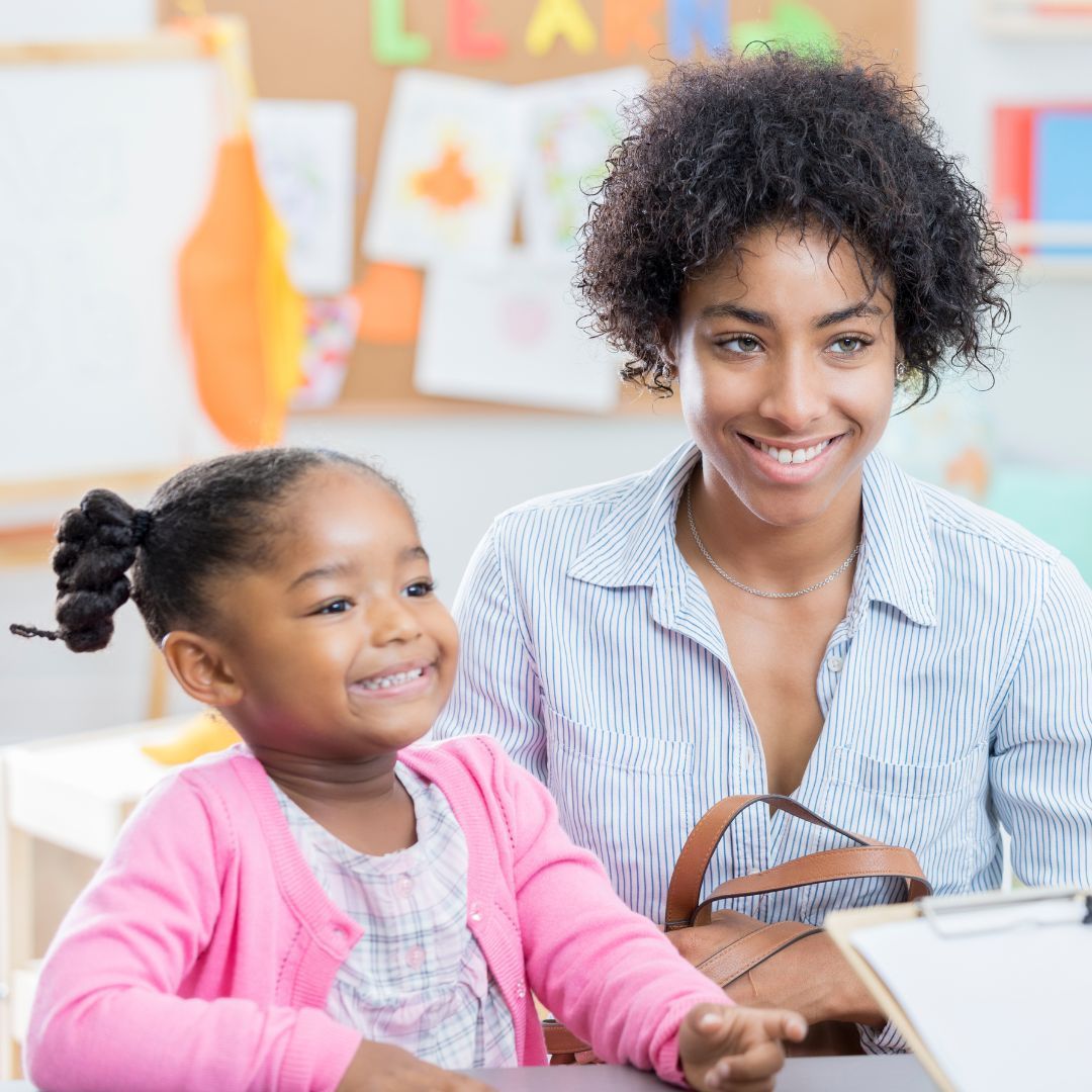 A woman and a little girl are sitting at a table in a classroom.