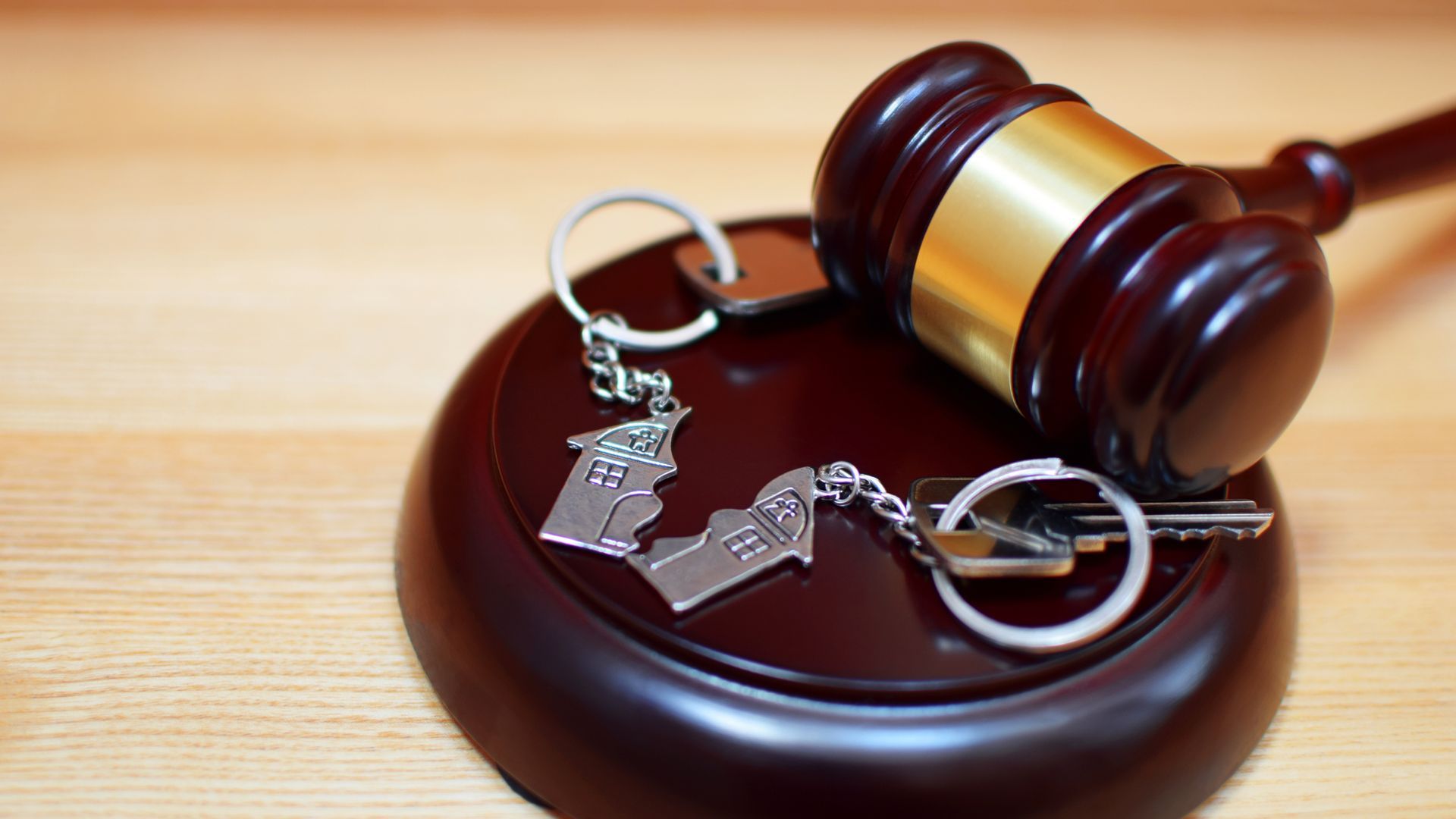two keys with a torn in half house on a wooden gavel and base