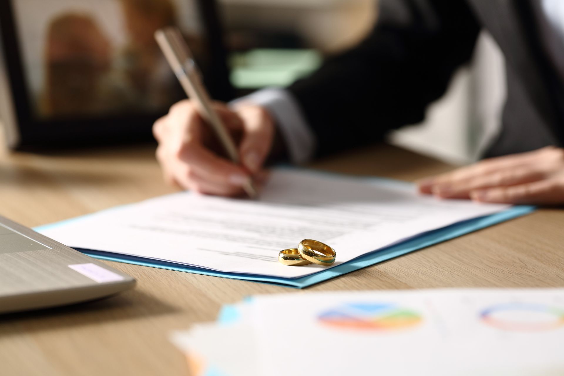 two wedding rings sitting atop a document, with someone signing them in the background
