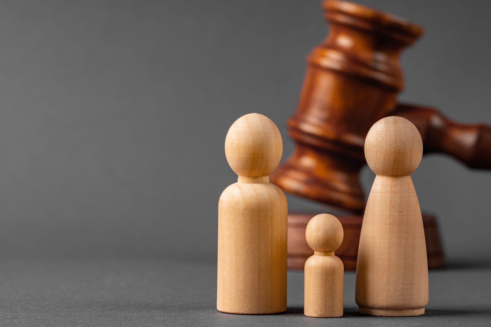 Three wooden figures in front of a gavel on a gray background