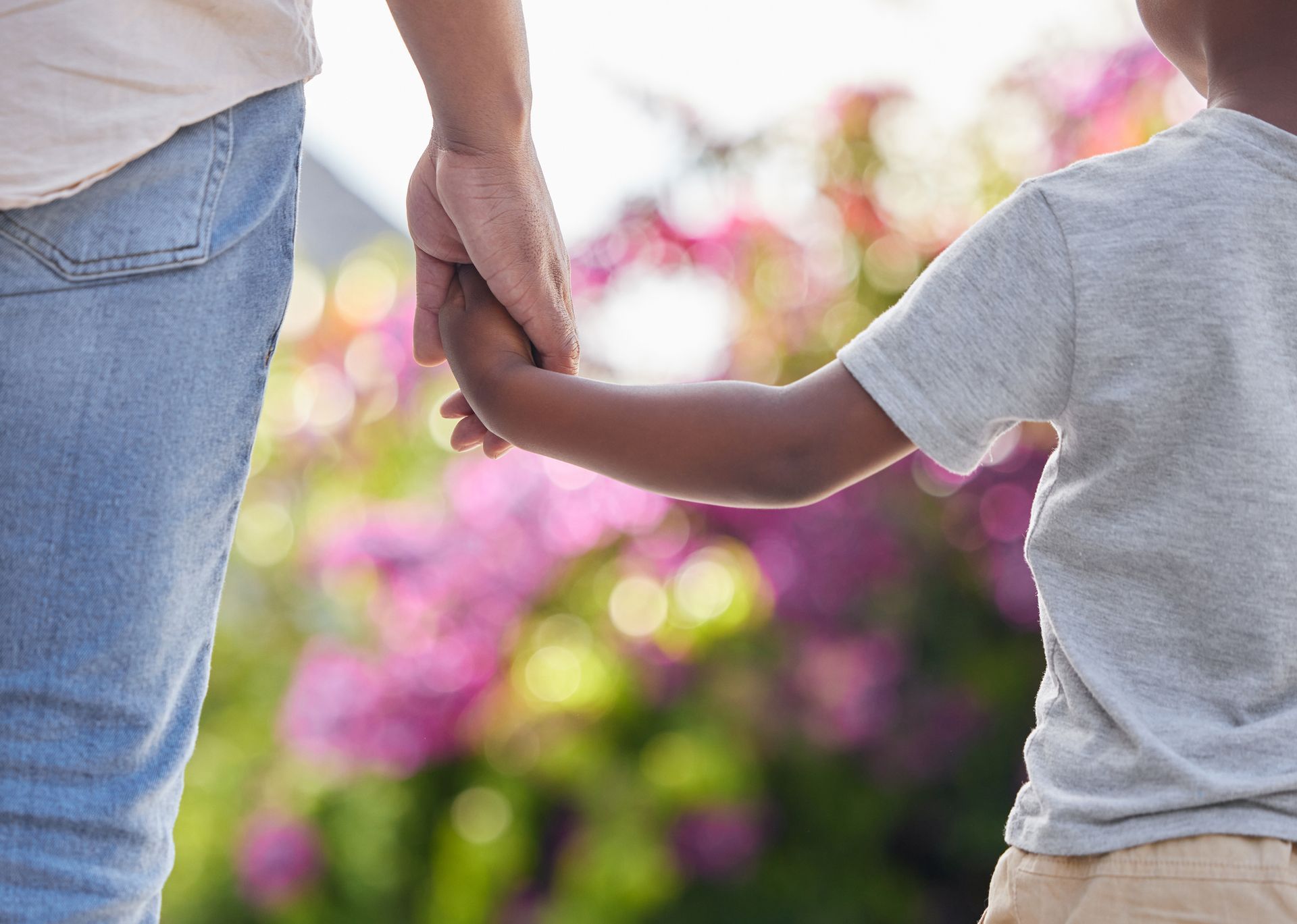 Adult and child holding hands outdoors with blurred pink flowers in the background