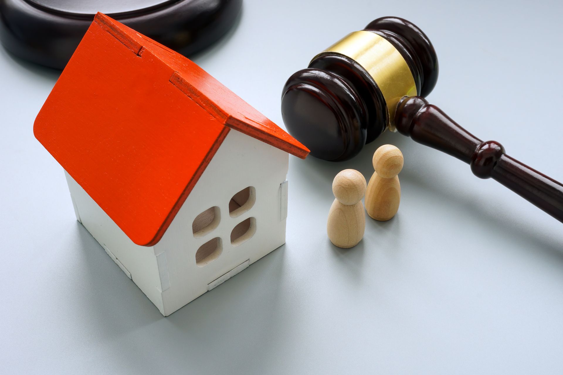 Miniature house with red roof beside a judge’s gavel and two wooden figures, suggesting a property dispute